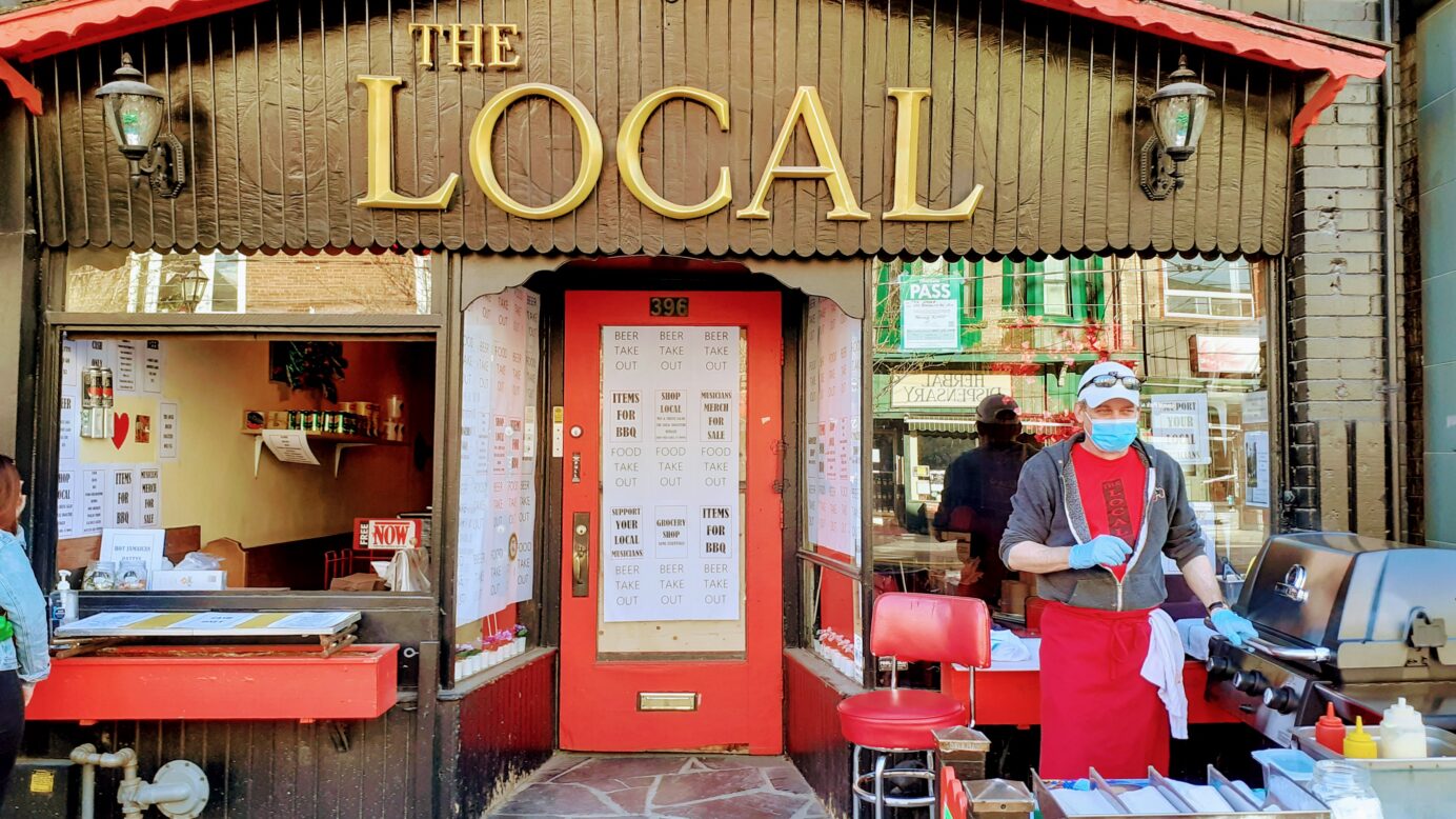 Masked chef prepares food in front of local pub, called The Local, during pandemic.